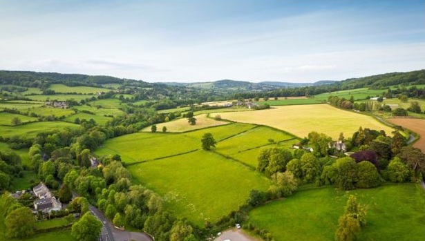 Aerial view of green fields, trees and rolling hills under a clear sky.